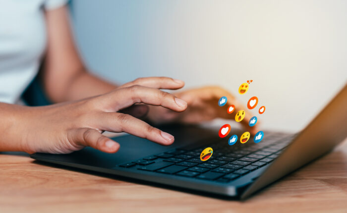 Hands using a laptop keyboard wich emits a series of reaction emoji's When talking about Brand Influence